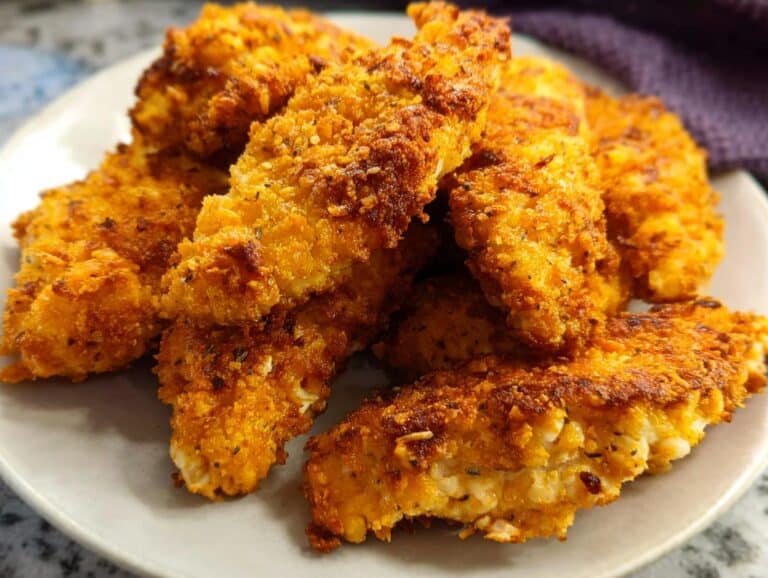 A close-up of several crispy, golden Air Fryer Chicken Parmesan Strips piled on a light gray plate.
