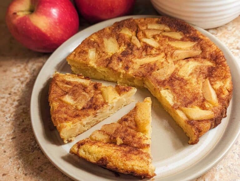 A sliced Apple Cinnamon Skillet Pancake on a plate, with apples in the background.