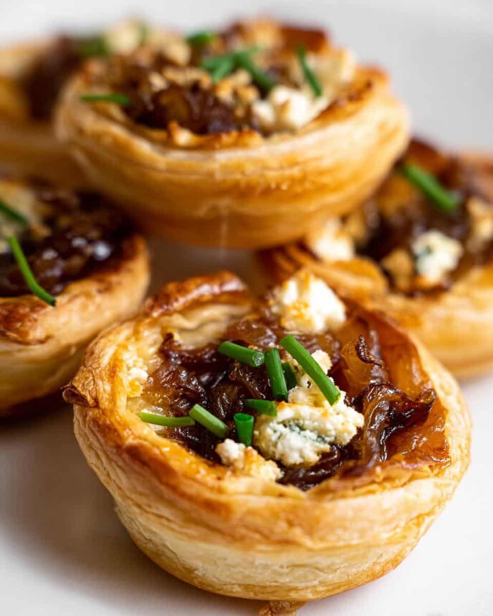 Close-up of flaky puff pastry Caramelized Onion Tartlets topped with blue cheese crumbles and fresh green chives.