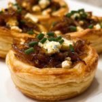 Close-up of three flaky puff pastry Caramelized Onion Tartlets topped with rich onions, blue cheese crumbles, and chives.