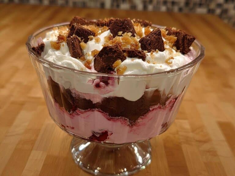 A layered Chocolate Cranberry Trifle in a glass bowl, topped with whipped cream and brownie pieces.