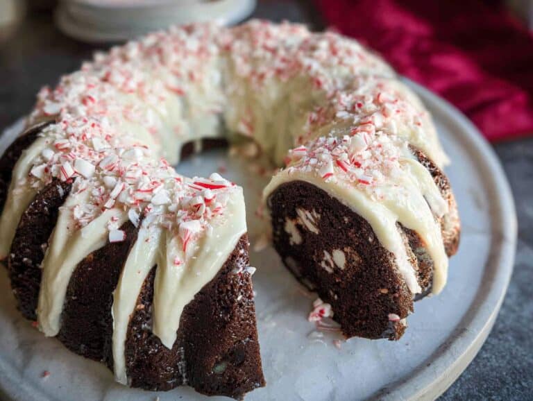 A chocolate peppermint bundt cake with white icing and crushed candy canes, with a slice removed.