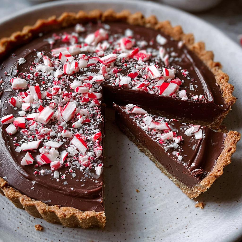 A delicious Chocolate Peppermint Tart with a slice cut out, revealing the creamy chocolate filling and peppermint candy topping.