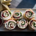 Six slices of Christmas Cranberry Turkey Roll Ups arranged on a platter next to a golden star decoration.