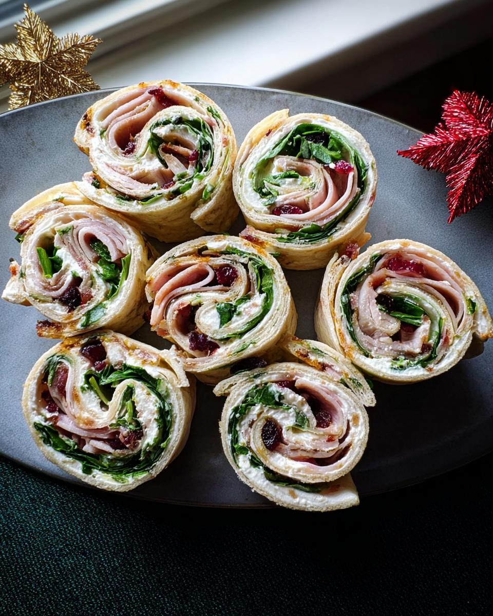Seven slices of Christmas Cranberry Turkey Roll Ups arranged on a dark plate, showing turkey, spinach, and cranberries.