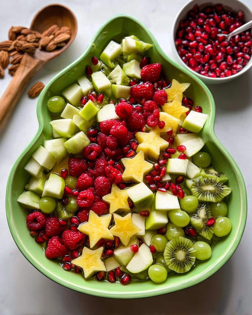 Overhead shot of Christmas Morning Fruit Salad in a tree-shaped bowl with raspberries, kiwi, starfruit, and pomegranate.