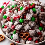 A close-up of a bowl filled with Christmas Puppy Chow, coated in powdered sugar and mixed with red and green M&Ms and small pretzels.