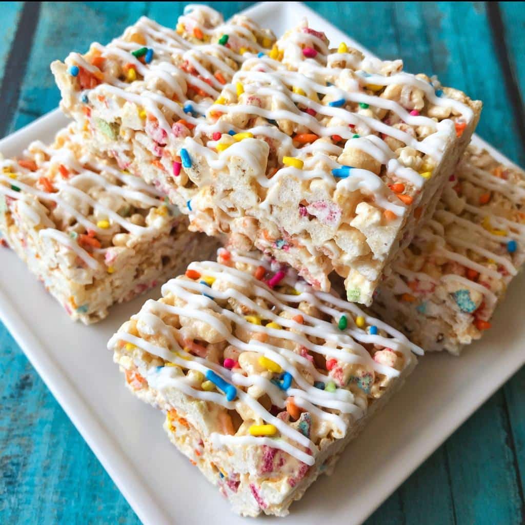 Four square servings of Funfetti Marshmallow Popcorn Treats drizzled with white icing and colorful sprinkles.