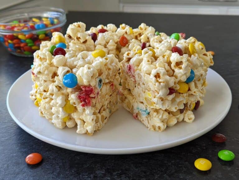 A square serving of Marshmallow Birthday Cake Popcorn, coated in marshmallow and studded with colorful M&M's, cut to show the interior.