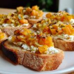 Close-up of several Pumpkin Goat Cheese Crostini appetizers featuring toasted bread, creamy goat cheese, and orange pumpkin topping.