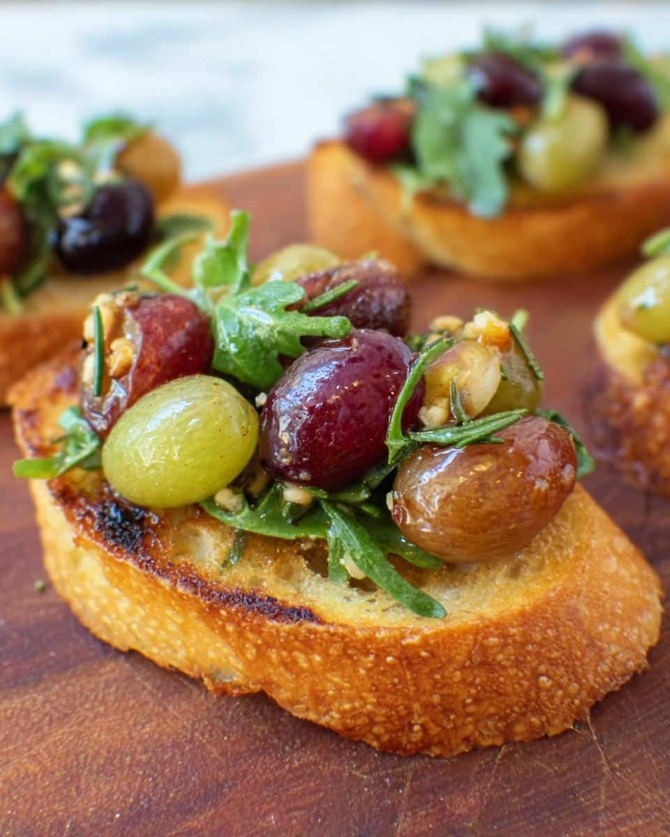Close-up of a single Roasted Grape & Rosemary Crostini topped with roasted red and green grapes, arugula, and rosemary.