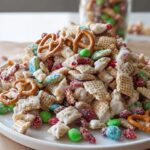 A mound of homemade Christmas Chex Mix featuring white chocolate coating, pretzels, and colorful candies.