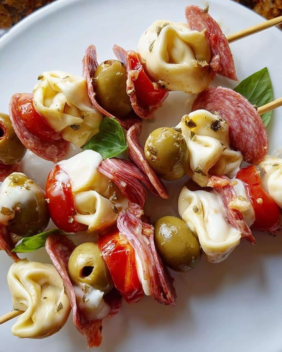 Close-up of two Antipasto Skewers featuring tortellini, green olives, salami, and red peppers on a white plate.