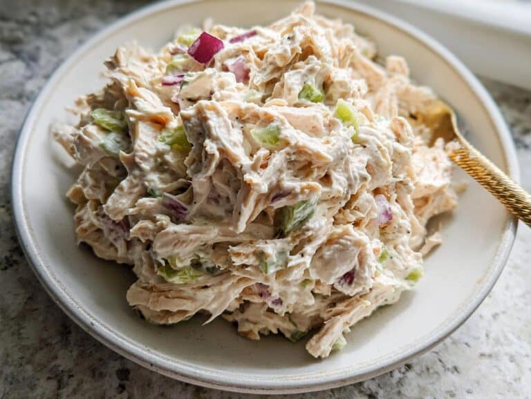 A close-up of creamy Cottage Cheese Chicken Salad piled high on a white plate with visible chunks of shredded chicken, celery, and red onion.