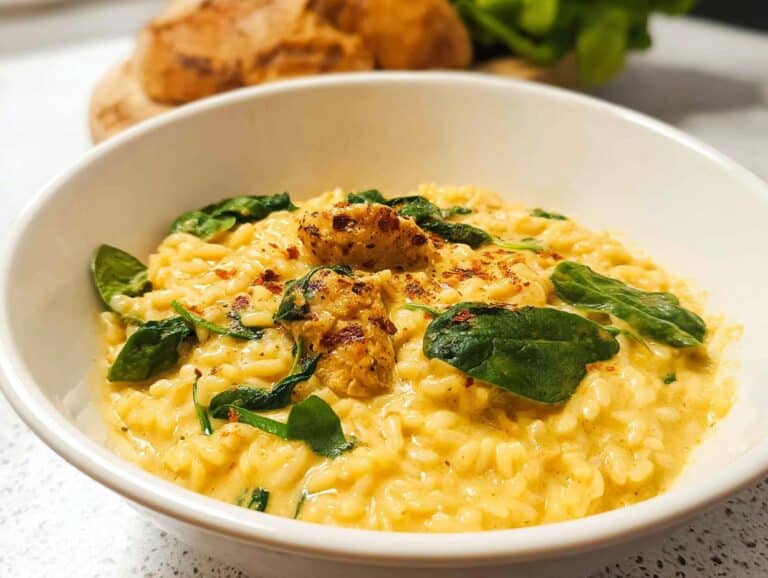 A close-up of creamy Lemon Chicken Thermomix Risotto topped with spinach and chicken pieces in a white bowl.