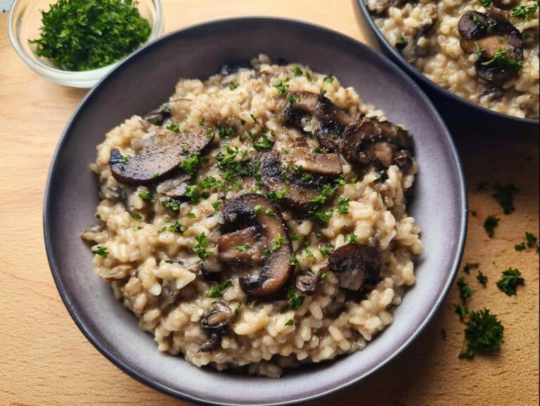 Close-up of a bowl filled with creamy vegan mushroom risotto, topped with sautéed mushrooms and fresh parsley.