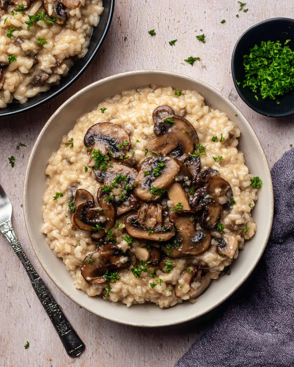 Overhead view of a bowl of creamy vegan mushroom risotto topped with sautéed mushrooms and fresh parsley.