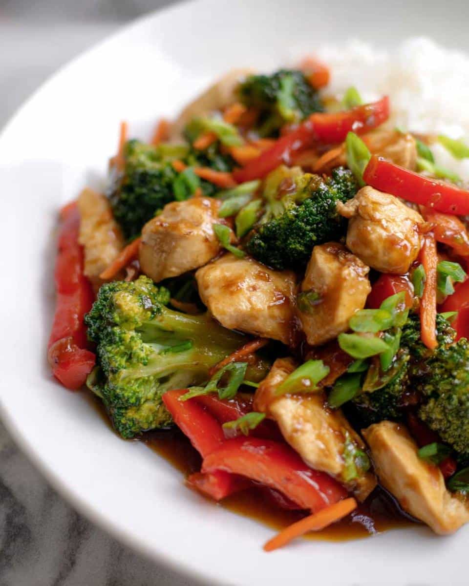 Close-up of a serving of Dairy-Free Gluten-Free Chicken Stir Fry with broccoli, red peppers, and sauce, next to white rice.