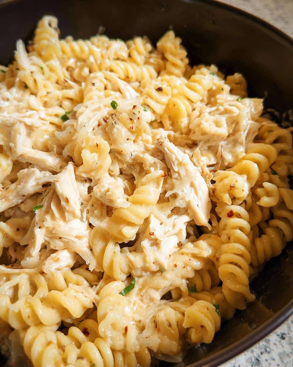 Close-up of creamy pasta mixed with shredded chicken, seasoned with herbs, representing Easy Crockpot Garlic Parm Chicken Pasta.