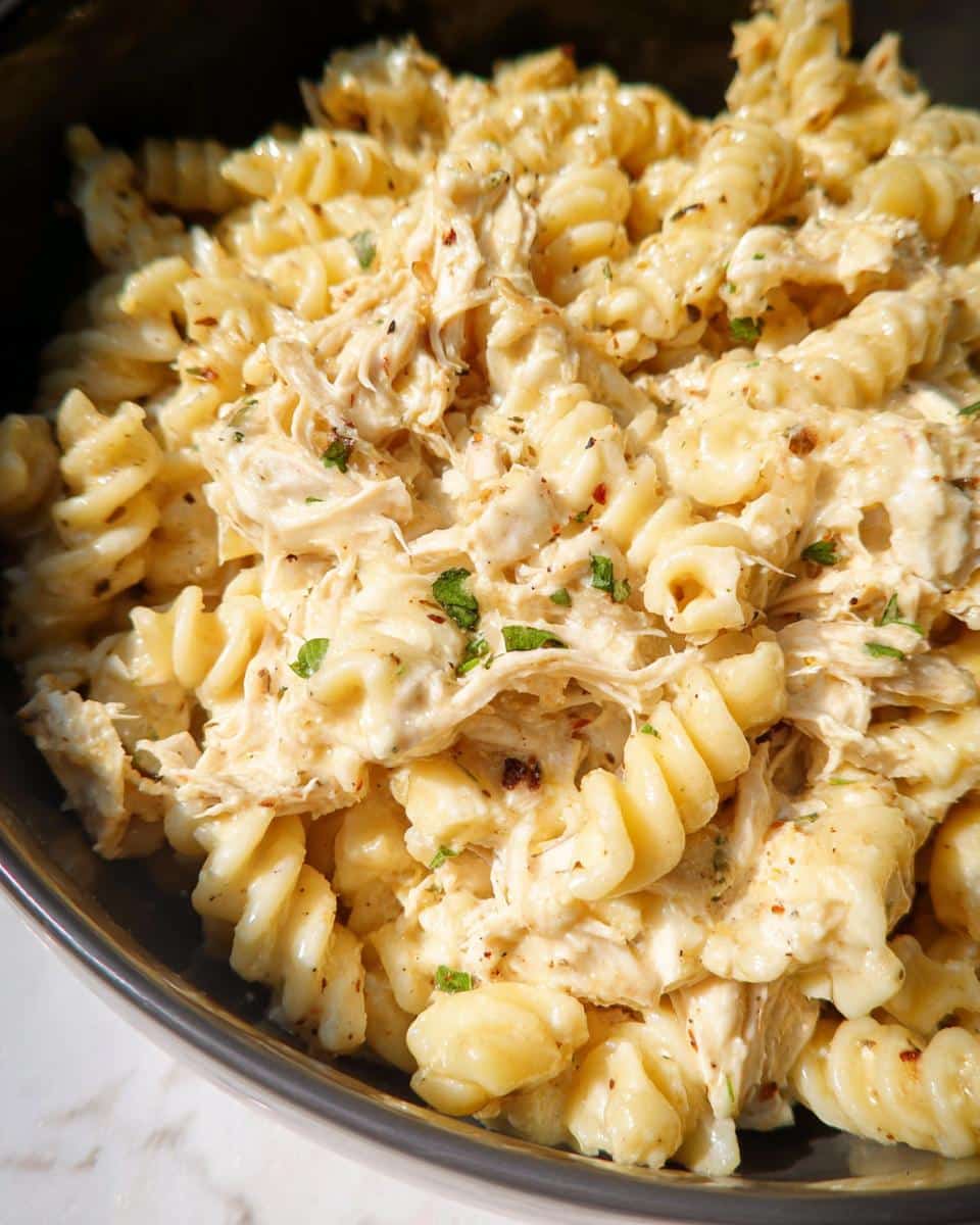 Close-up of creamy Easy Crockpot Garlic Parm Chicken Pasta with shredded chicken and fusilli pasta.