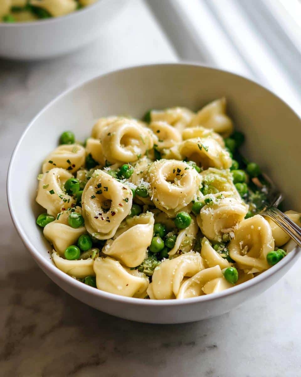 Close-up of Garlic Butter Tortellini with Peas, topped with Parmesan and herbs, served in a white bowl.