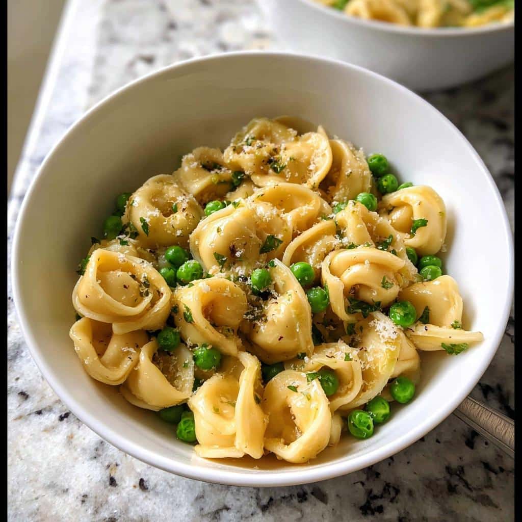 Close-up of Garlic Butter Tortellini with Peas, topped with Parmesan cheese and parsley in a white bowl.