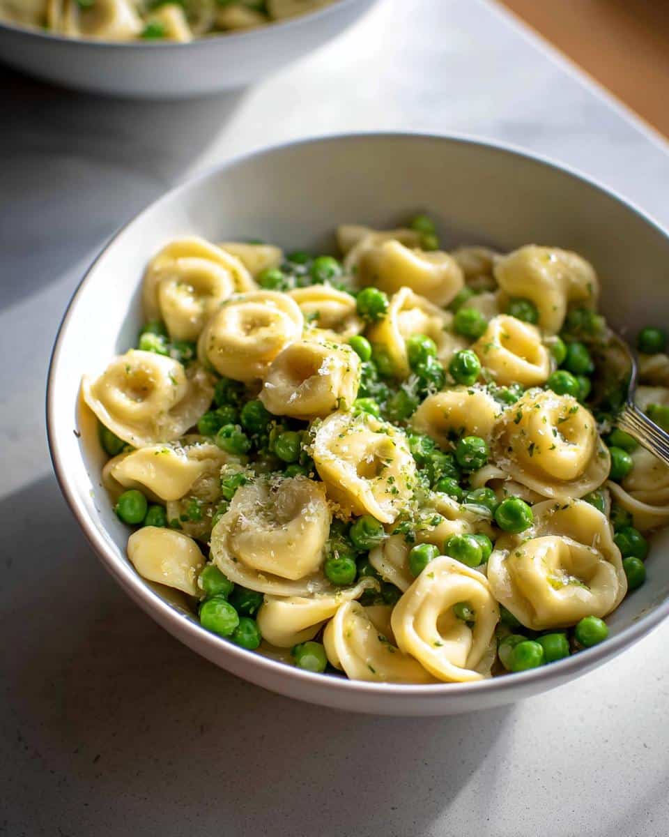 A close-up of Garlic Butter Tortellini with Peas, topped with Parmesan cheese and herbs, served in a white bowl.