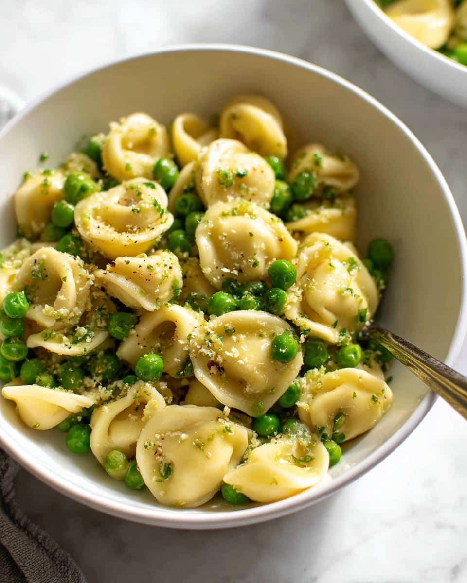 Close-up of Garlic Butter Tortellini with Peas tossed in a light sauce and topped with herbs in a white bowl.