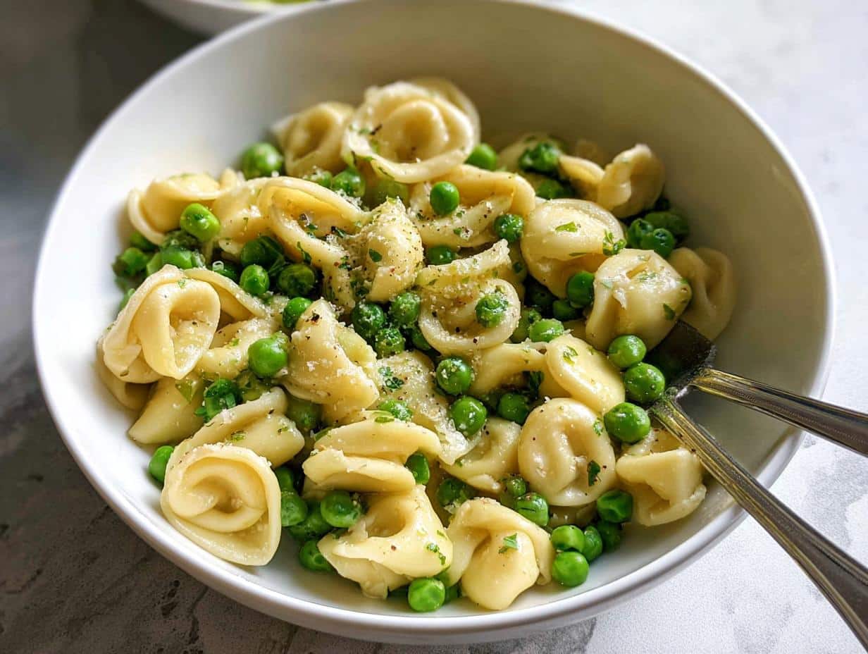 Close-up of Garlic Butter Tortellini with Peas tossed in a white bowl, garnished with cheese and herbs.