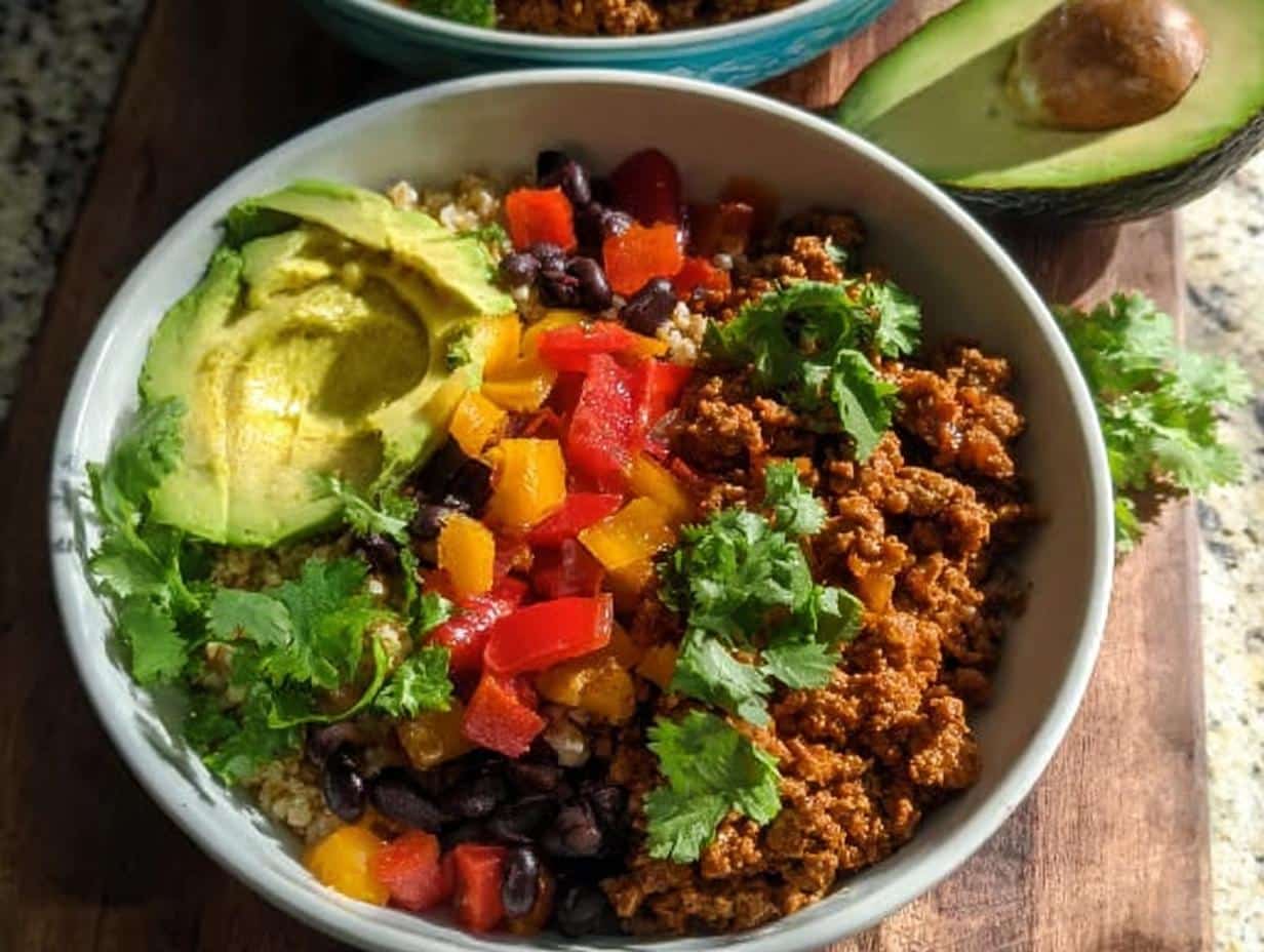 A close-up of a Healthy Taco Bowl featuring seasoned ground meat, black beans, peppers, avocado slices, and cilantro.