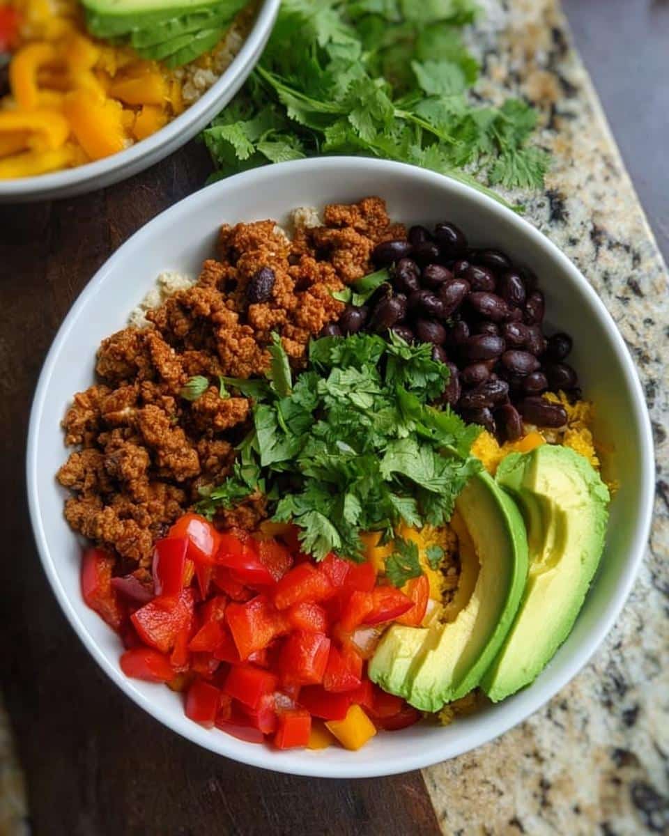 Overhead view of a vibrant Healthy Taco Bowl featuring seasoned ground meat, black beans, avocado slices, and fresh cilantro.