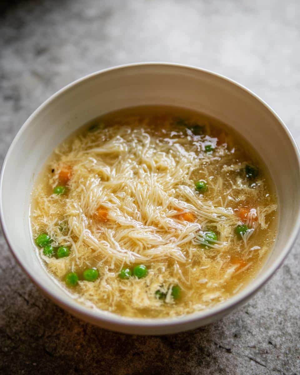 Close-up of a bowl of High-Protein Egg Drop Soup featuring thin noodles, egg ribbons, peas, and carrots.