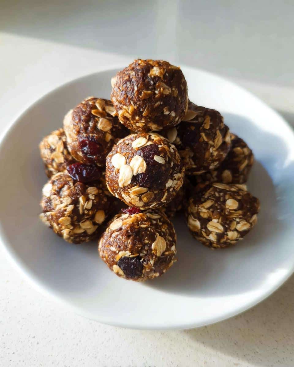 A stack of homemade No-Bake Energy Balls, visible with rolled oats and dried cranberries, served on a white plate.
