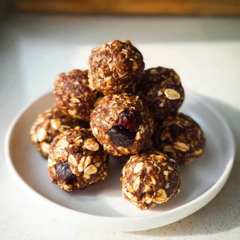 A stack of homemade No-Bake Energy Balls made with oats and visible dried fruit, served on a small white plate.