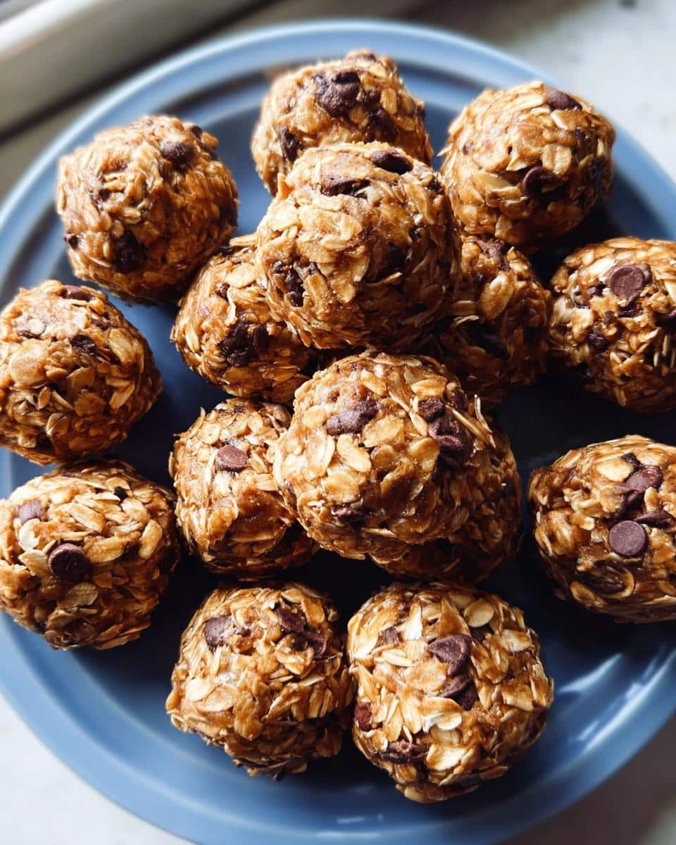 A close-up of several homemade no-bake protein ball snacks covered in oats and chocolate chips on a blue plate.