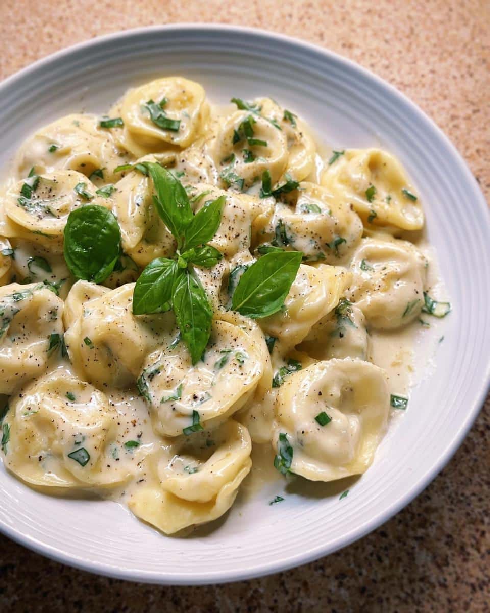 A close-up of tortellini pasta coated in a rich, creamy sauce, garnished with fresh basil and black pepper, highlighting the One-Pot Creamy Tortellini with Basil.