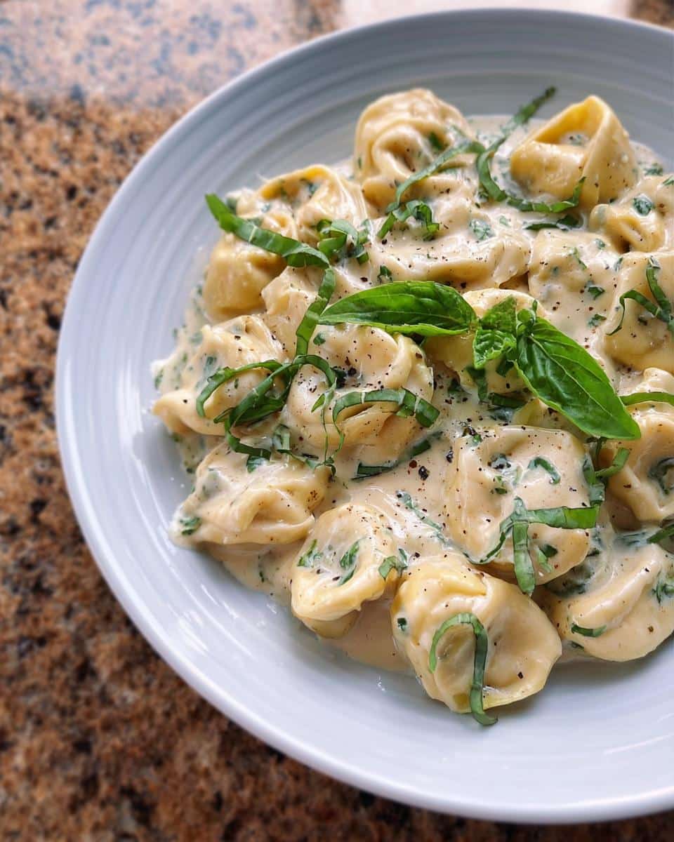 Close-up of a white bowl filled with One-Pot Creamy Tortellini with Basil, garnished with fresh basil leaves and pepper.