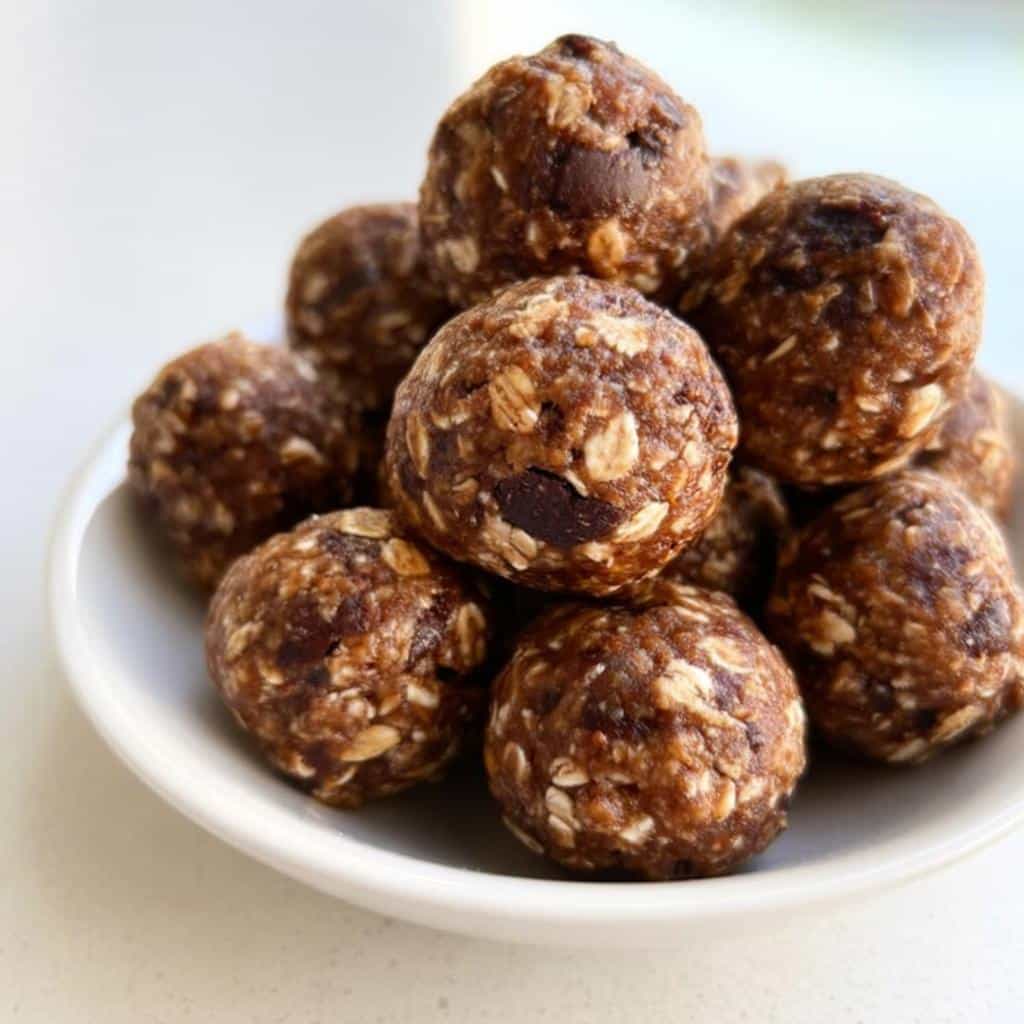 A close-up of several delicious Peanut Butter Chocolate Energy Bites stacked in a small white bowl.