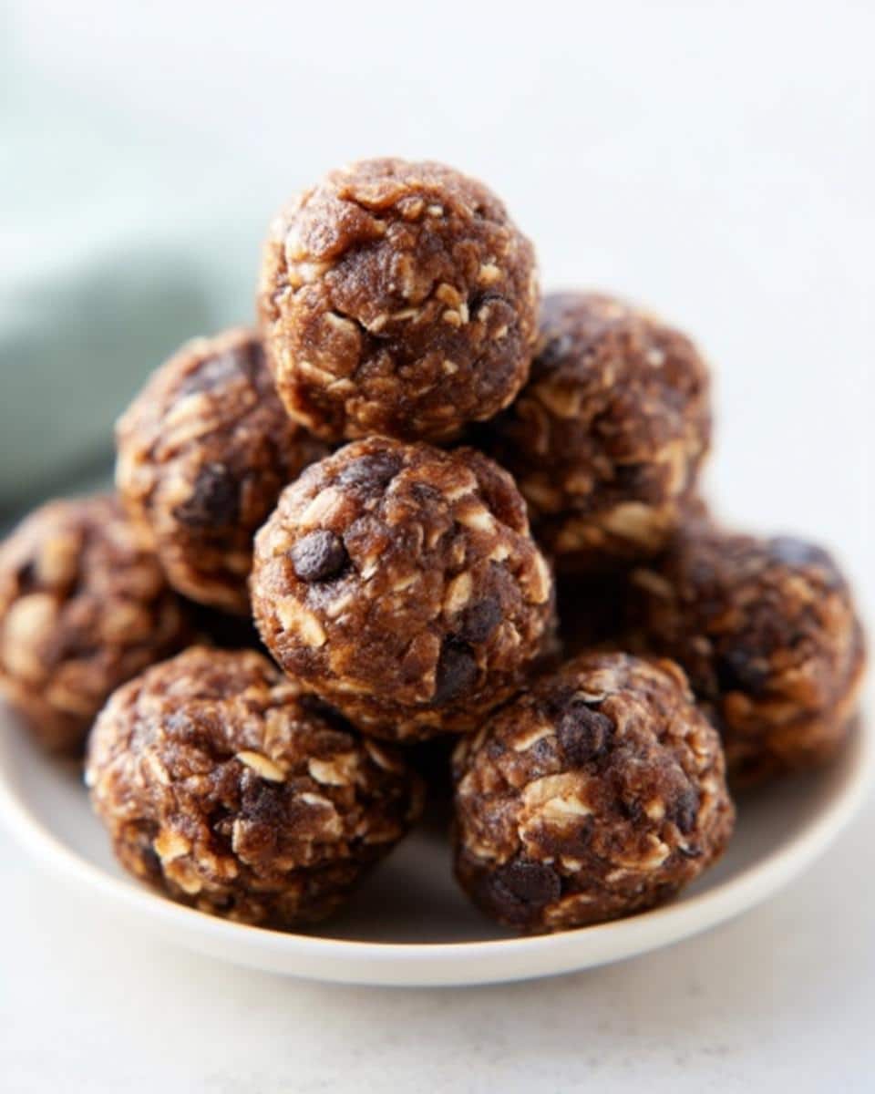 A stack of homemade Peanut Butter Chocolate Energy Bites featuring visible oats and chocolate chips on a white plate.