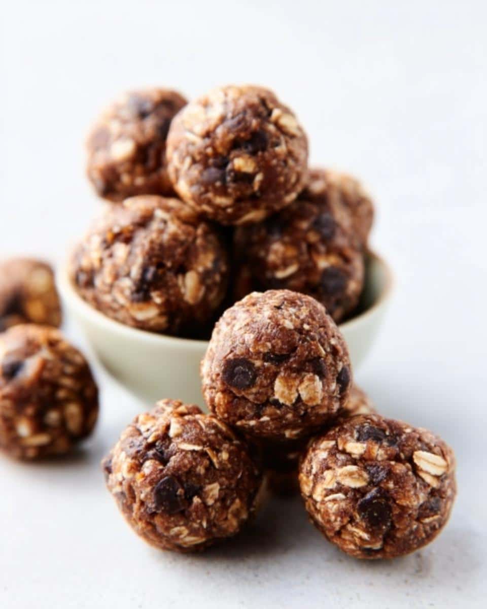 A close-up of stacked and scattered Peanut Butter Chocolate Energy Bites featuring oats and chocolate chips.