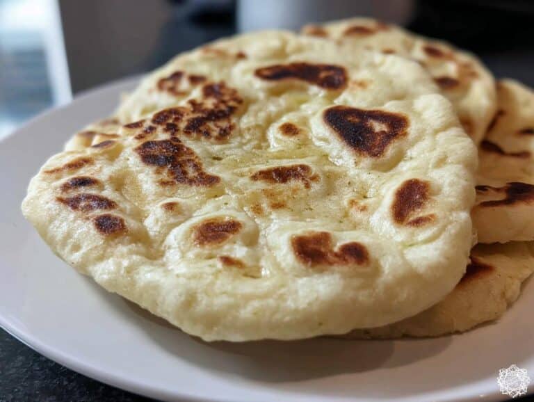 Close-up of several soft, freshly cooked Thermomix Naan breads stacked on a white plate, showing charred spots.