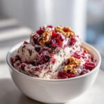 A white bowl filled with creamy Spiced Cranberry & Walnut Cheese Spread, topped with dried cranberries and walnuts.