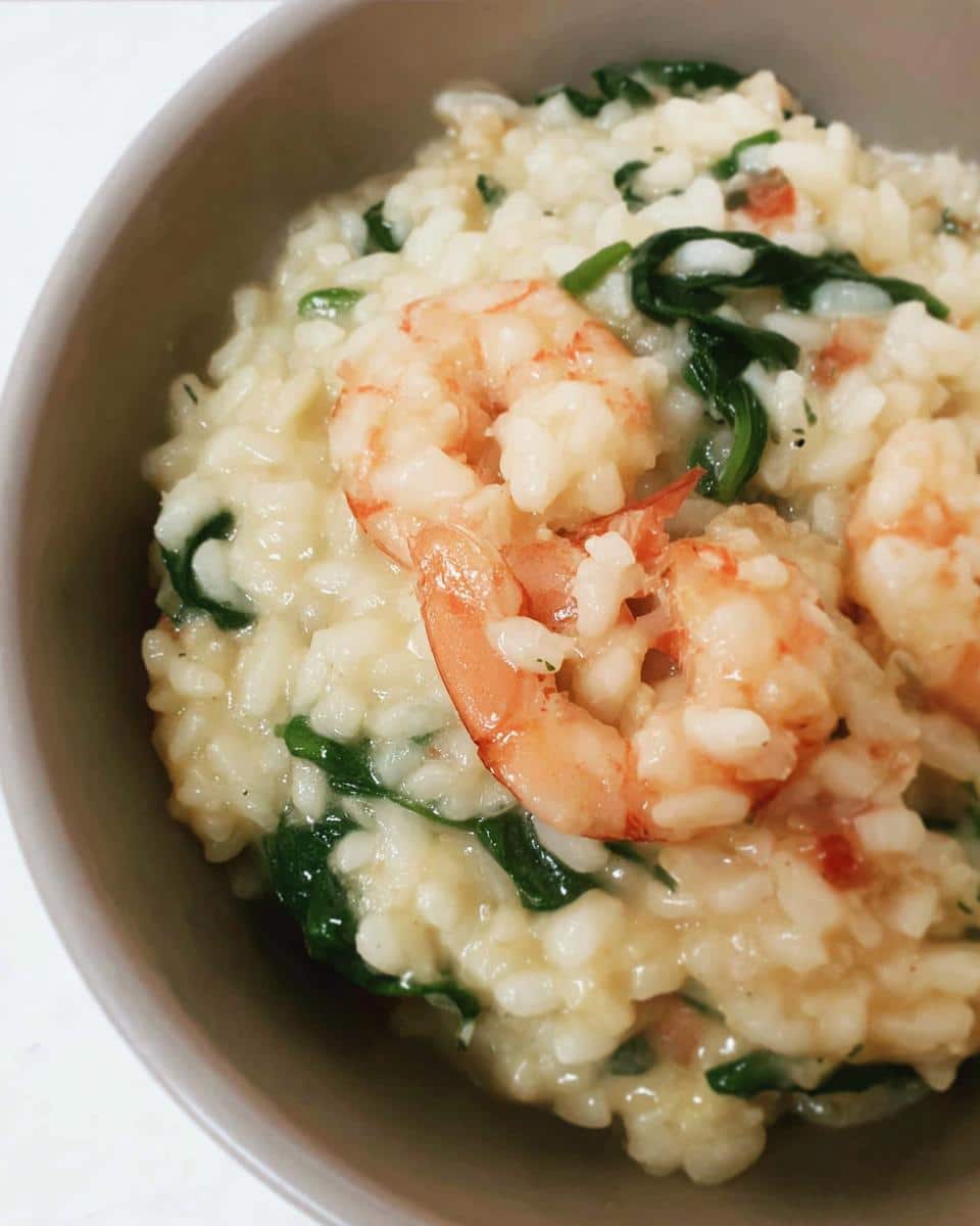 Close-up of creamy Thermomix Garlic Prawn Risotto topped with pink prawns and wilted spinach.