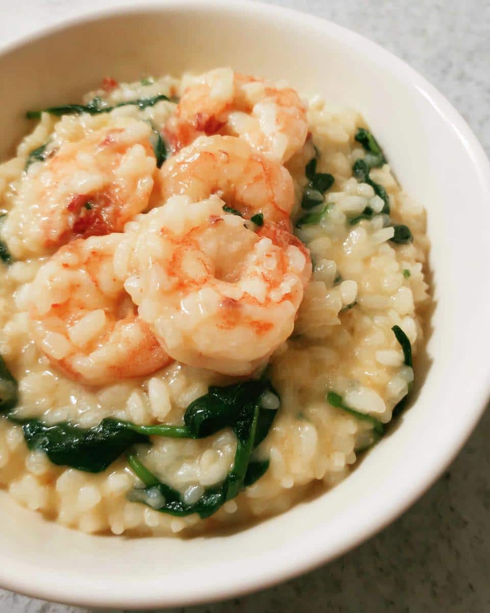 Close-up of creamy Thermomix Garlic Prawn Risotto topped with pink shrimp and wilted spinach in a white bowl.