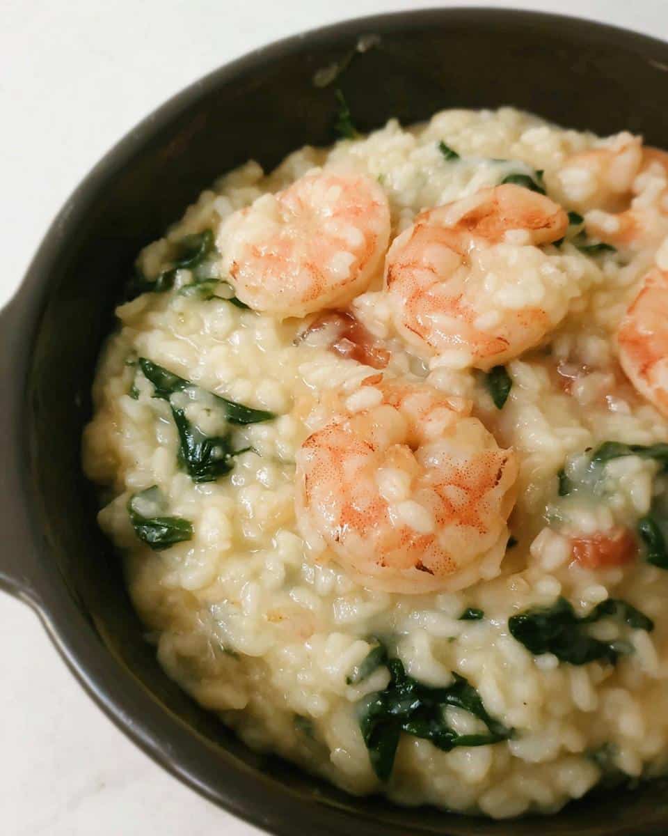 Close-up of creamy Thermomix Garlic Prawn Risotto topped with pink shrimp and wilted spinach in a dark bowl.