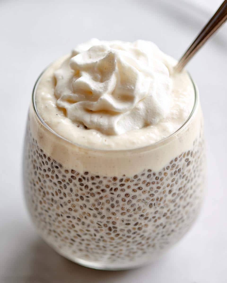 Close-up of Vanilla Keto Chia Pudding in a glass, topped with a swirl of whipped cream and a spoon.