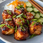 Close-up of glazed Air Fryer Gluten Free Salmon Bites topped with sesame seeds and green onions, served with rice and cucumbers.