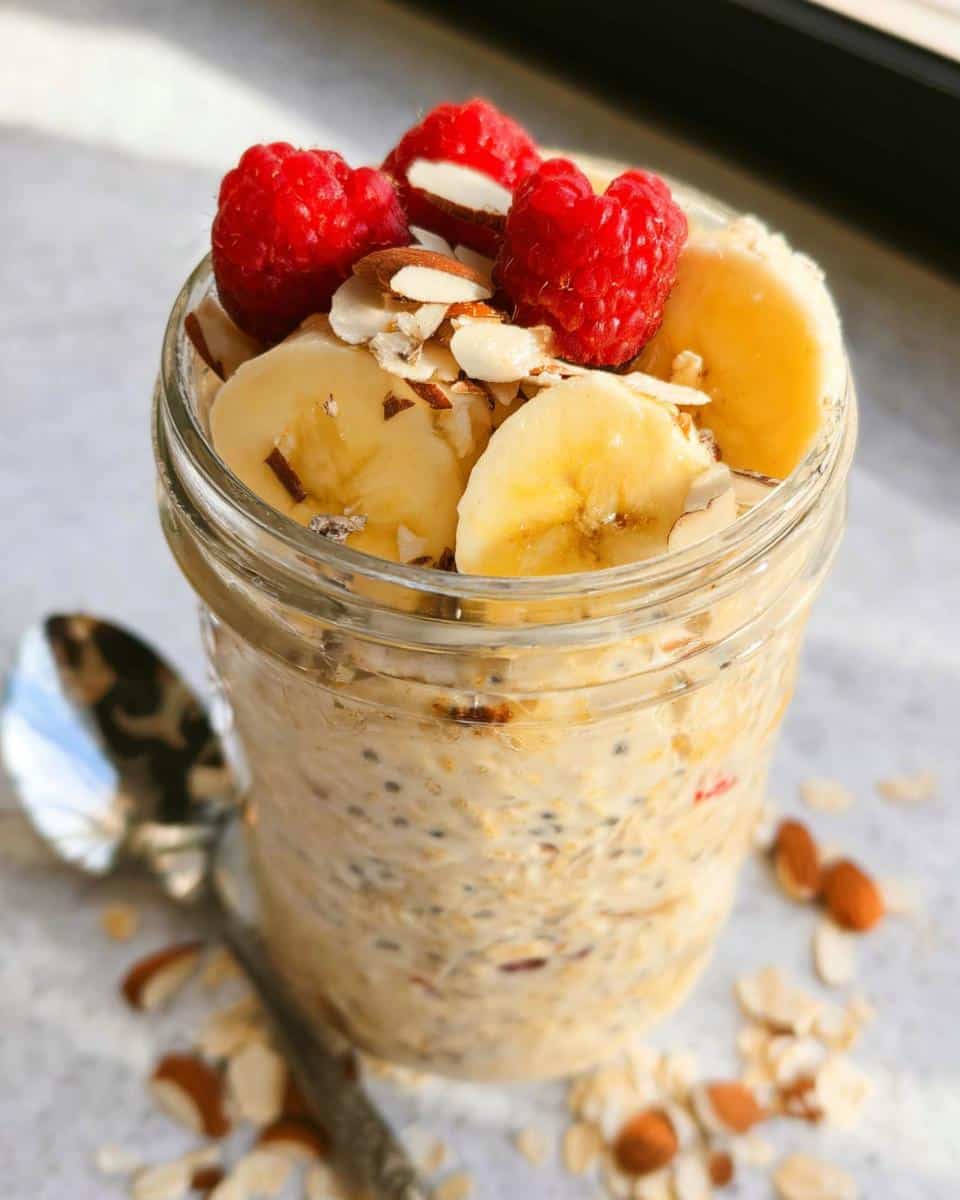 Close-up of Banana Almond Overnight Oats topped with fresh raspberries, banana slices, and slivered almonds.