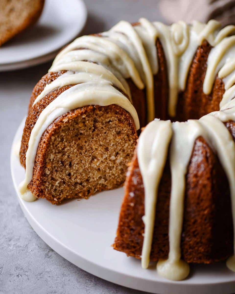 A rich, moist Banana Bread Bundt Cake drizzled with thick white glaze, featuring one slice cut out to show the crumb texture.