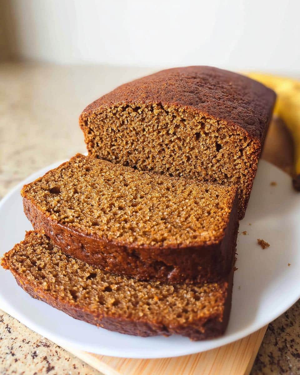 Close-up of a dark brown Banana Bread Espresso loaf, partially sliced on a white plate.